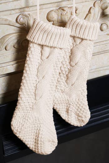 Two cream-colored cable-knit stockings hanging from a mantel, perfect for holiday decor