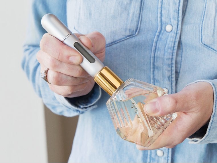 model holding the long silver atomizer on top of a bottle of perfume filling it