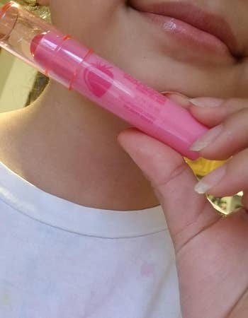 reviewer with subtle pink, glossy lips holding up the pink balm stick 