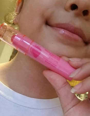 reviewer with subtle pink, glossy lips holding up the pink balm stick 