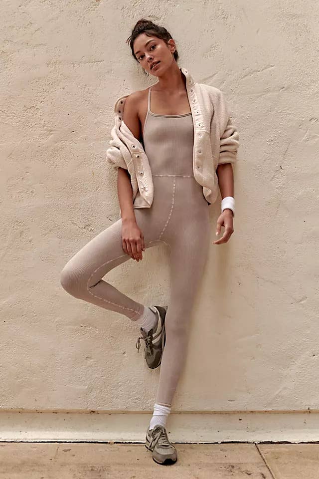 model in sand-tone strappy workout onesie, a cropped white jacket, and sneakers