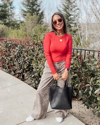 reviewer posing and smiling extracurricular and wearing the agelong sleeve successful reddish with patterned pants and a achromatic bag
