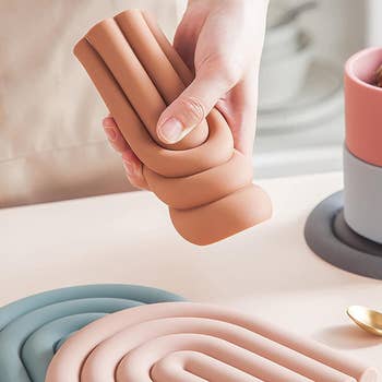 Hand holding a flexible silicone trivet in a coiled design, suitable for kitchen use