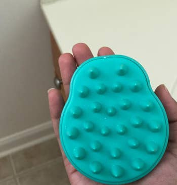 reviewer holding a teal silicone brush with massage points