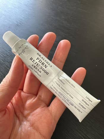 A hand holds a tube of Dr. Althea PDRN Repair 5000 Cream, suggesting skincare focus