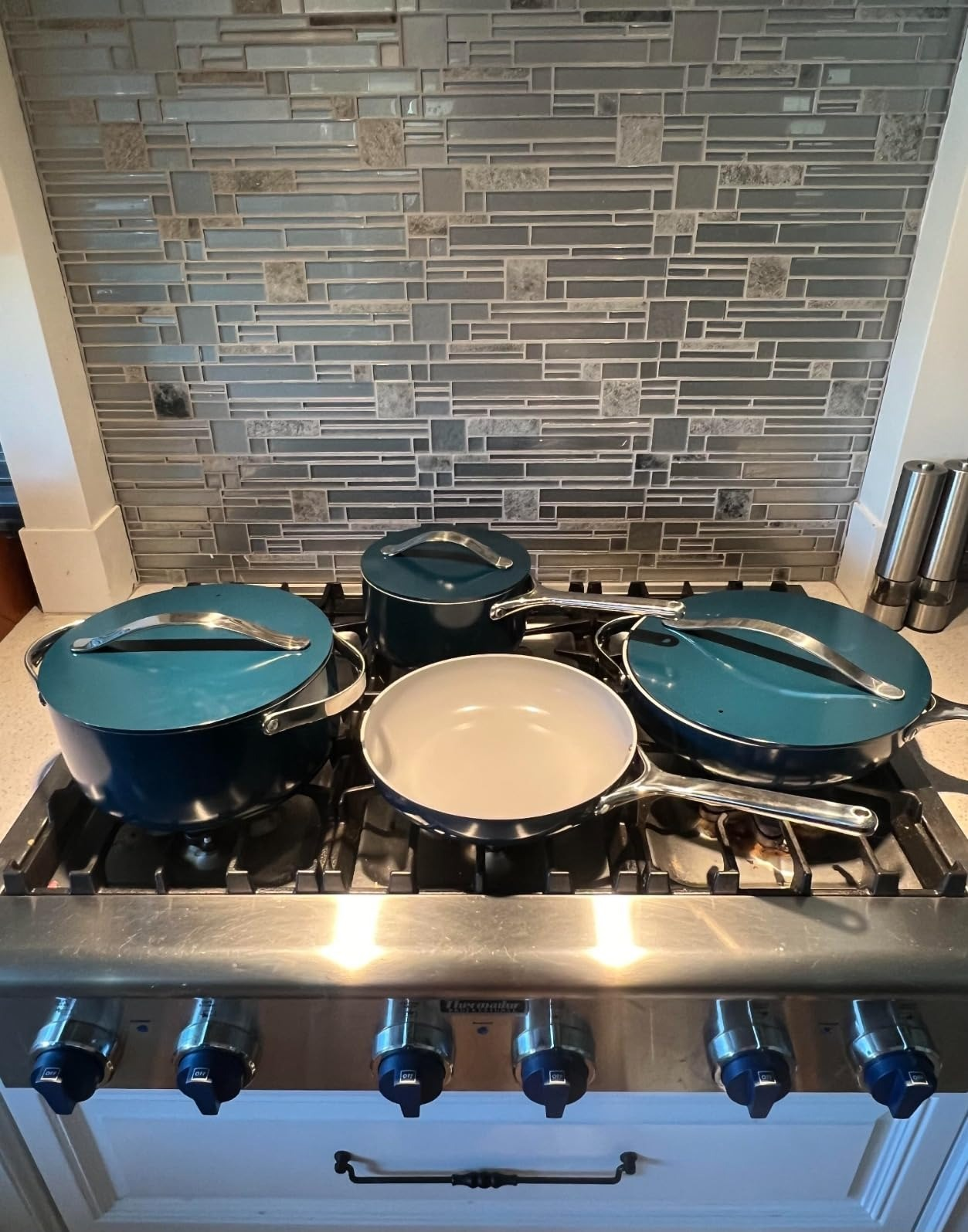 Four pots and pans with lids connected  a stainless alloy  stove, successful  beforehand   of a tiled backsplash, suggesting a room  setting