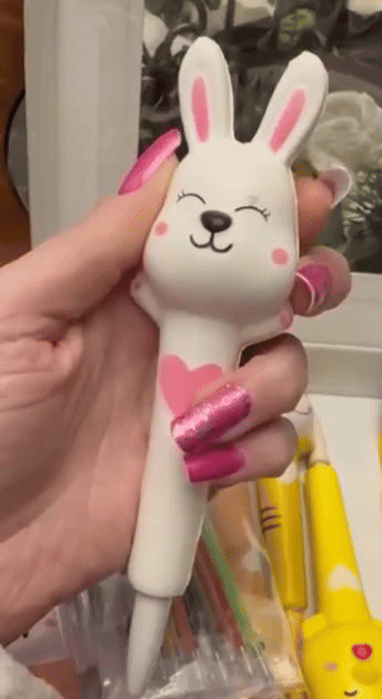 Hand holding a bunny-shaped pen with a heart design, surrounded by other colorful novelty pens, perfect for gifts or stationery collection