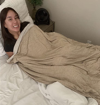 reviewer in bed covered with the tan blanket