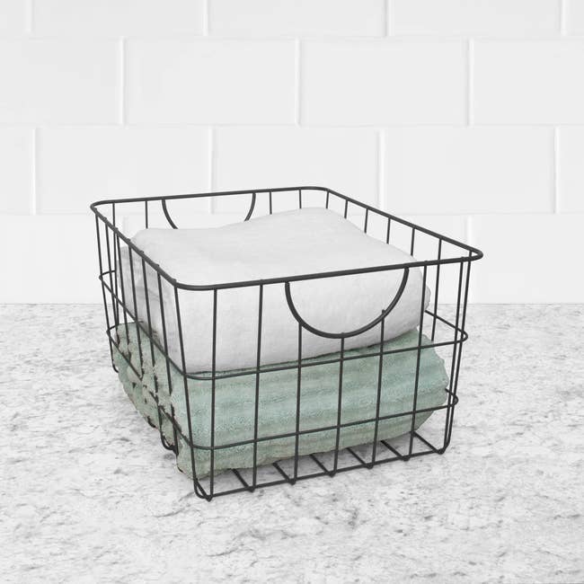Wire storage basket holding folded towels, set on a marble countertop