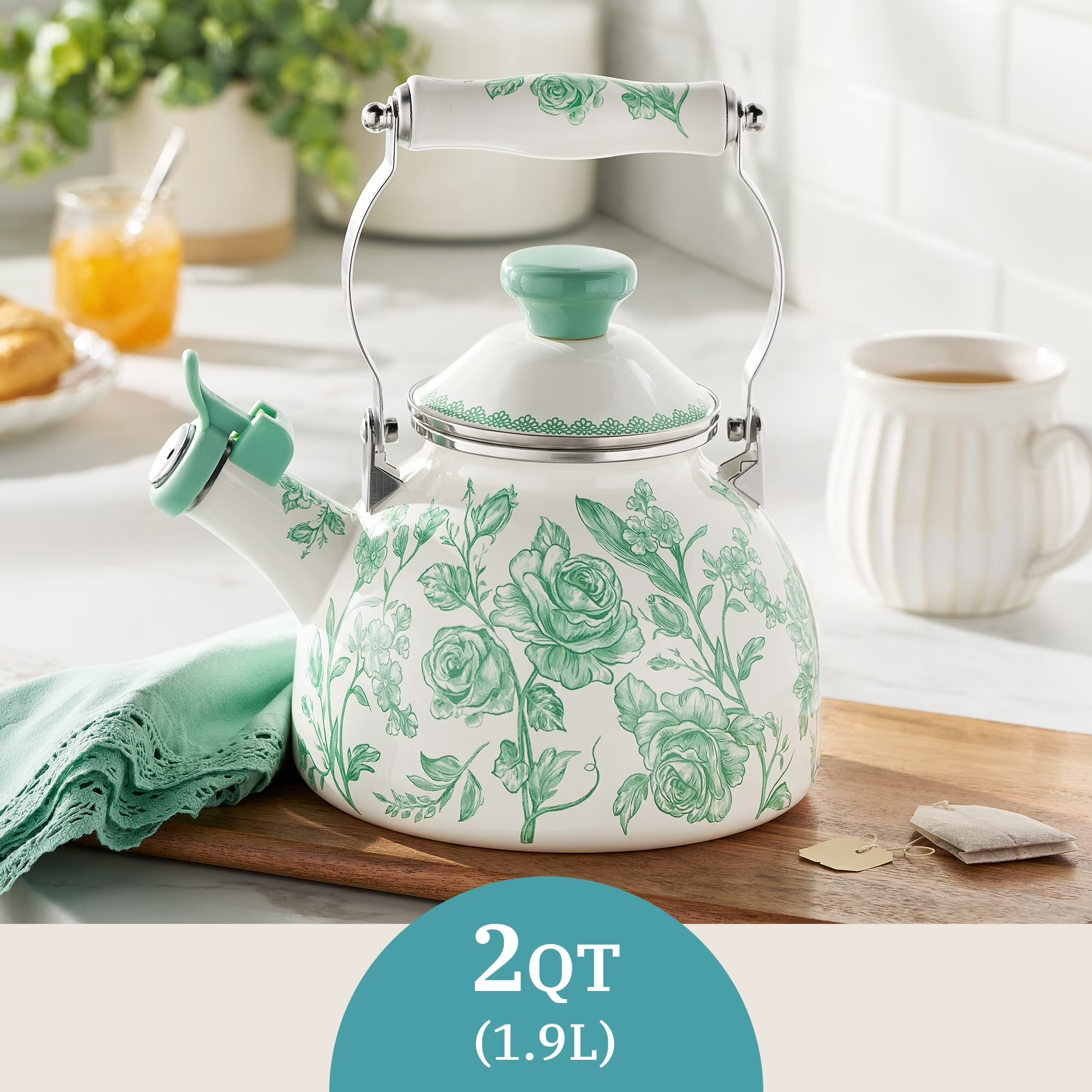 Floral-patterned 2-quart (1.9L) teapot connected  a room  counter, adjacent  to beverage  items and a greenish  cloth