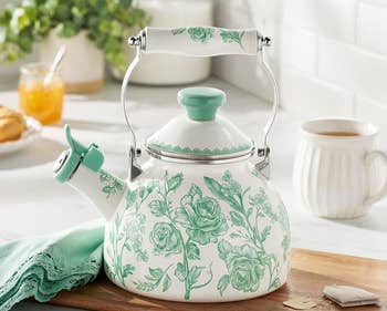 Floral-patterned 2-quart (1.9L) teapot connected a room counter, adjacent to beverage items and a greenish cloth