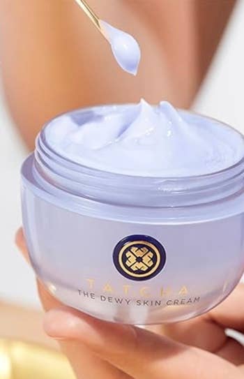 Close-up of a hand holding a jar of Tatcha Dewy Skin Cream with a dropper dispensing the product