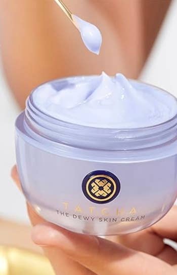 Close-up of a manus  holding a jar of Tatcha Dewy Skin Cream with a dropper dispensing the product