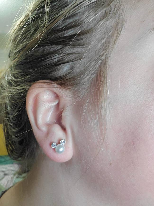 a reviewer wearing the pearl earrings with the two sparkling studs to make a mouse ear