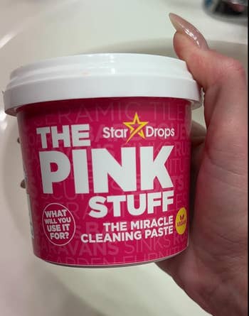 Hand holding a container of The Pink Stuff cleaning paste