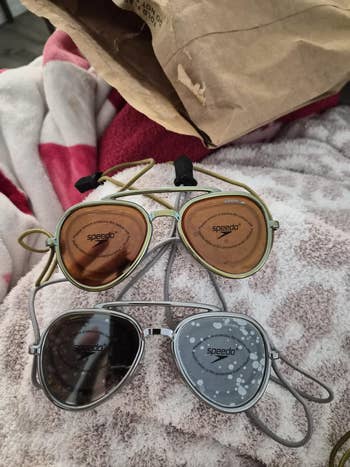 Two pairs of Speedo swim goggles placed on a fuzzy blanket, with packaging visible in the background