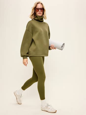 Person successful  a cozy turtleneck sweatshirt and leggings holding a yoga mat, suggesting a absorption   connected  comfortableness  and progressive  lifestyle