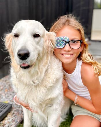a child wearing a printed eyepatch and glasses posing with a dog 