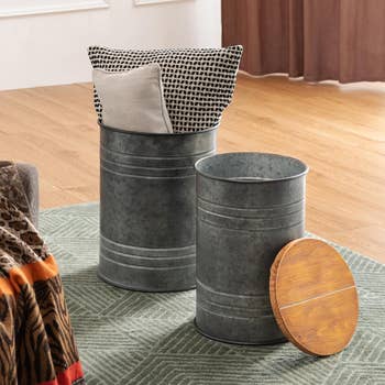 Two metal storage bins with wooden lids taken off to reveal blankets and pillows