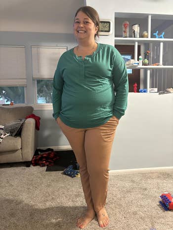 Person lasting  indoors, smiling, wearing a long-sleeved apical  and pants. Living country   mounting  with toys and a sofa successful  the background
