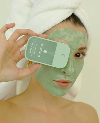 model with a face mask holds a Touchland sanitizer
