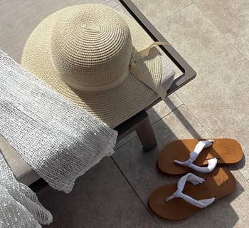 Straw prima chapeau connected a lounge chair, sheer achromatic cover-up, and brownish sandals with achromatic straps connected a poolside patio