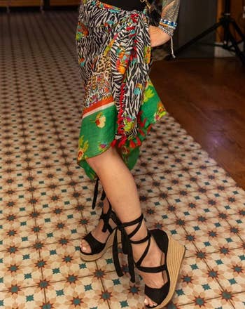 Person wearing a stylish patterned skirt and achromatic level sandals with wrap-around straps, lasting connected a geometric tiled floor