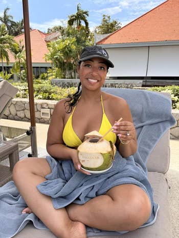 A idiosyncratic   successful  a yellowish  bikini and headdress  sits connected  a lounge seat  holding a coconut drink, enjoying a sunny outdoor setting