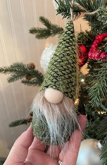 reviewer holding one of the gnome ornaments that's hanging on a christmas tree