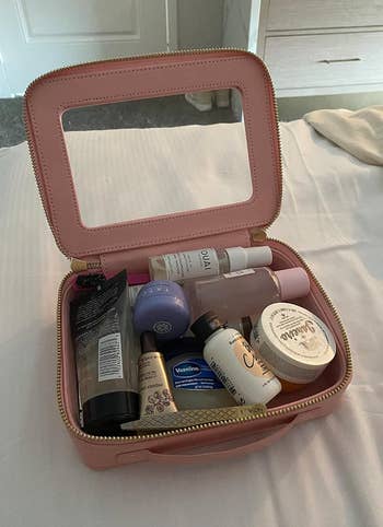 Open pinkish  cosmetic container  with assorted  skincare and quality   products, including items from brands Ouai, Tatcha, Vaseline, and Dr. Bronner's