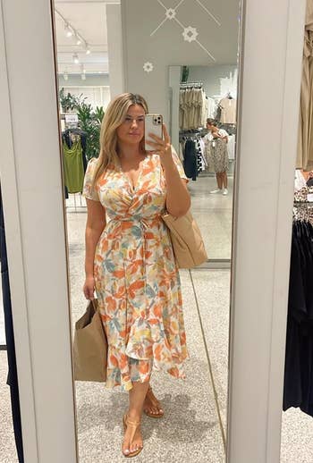 reviewer in a floral dress posing with shopping bags in a clothing store mirror