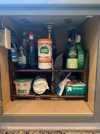 reviewer showing the cabinet under their kitchen sink after using the two-tier expandable shef with everything neat and organized