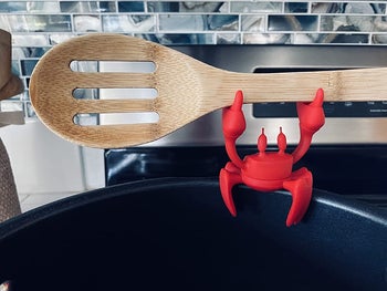 reviewer close-up of the silicone crab spoon rest holding a wooden spoon 