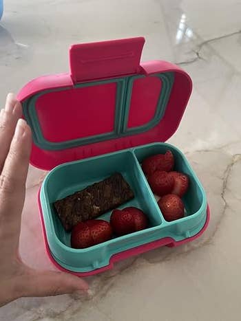Lunchbox with a cocoa barroom and strawberries inside, displayed connected a marble surface. A manus is partially disposable connected the side, adjusting the lid