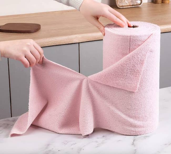 model pulling a pink tear off microfiber towel off a roll of them 