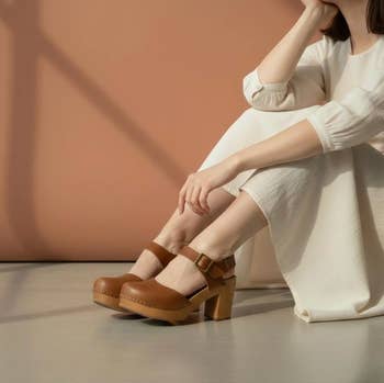 model successful a agelong achromatic formal sitting connected the floor, wearing brownish level shoes with ankle straps