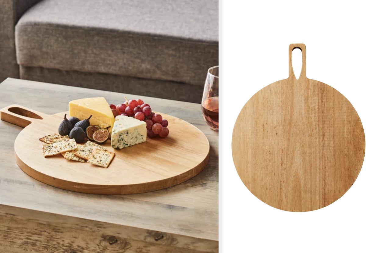 Light wooden circular charcuterie board with handle and cutout in center of handle on top of wooden table with food on top, product on a white background 
