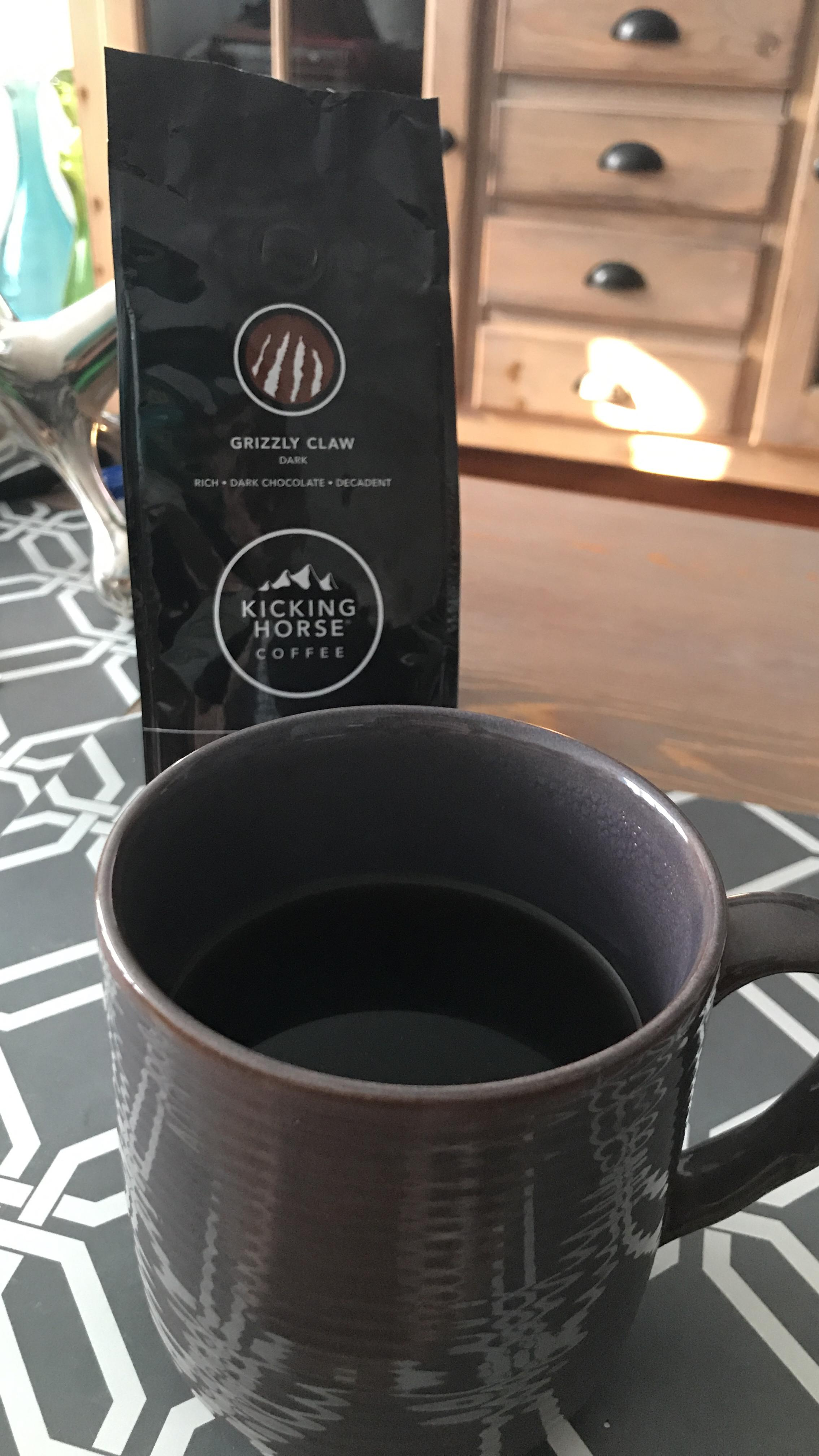 Coffee mug and a container  of Kicking Horse Coffee's Grizzly Claw blend, known for its rich, acheronian  cocoa  flavor, connected  a geometric-patterned table