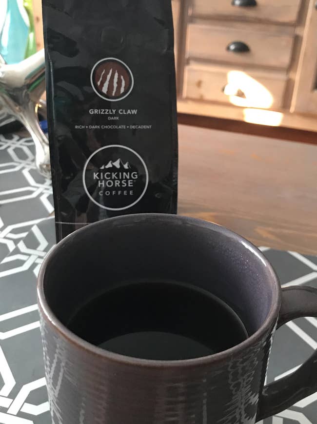 Coffee mug and a container of Kicking Horse Coffee's Grizzly Claw blend, known for its rich, acheronian cocoa flavor, connected a geometric-patterned table