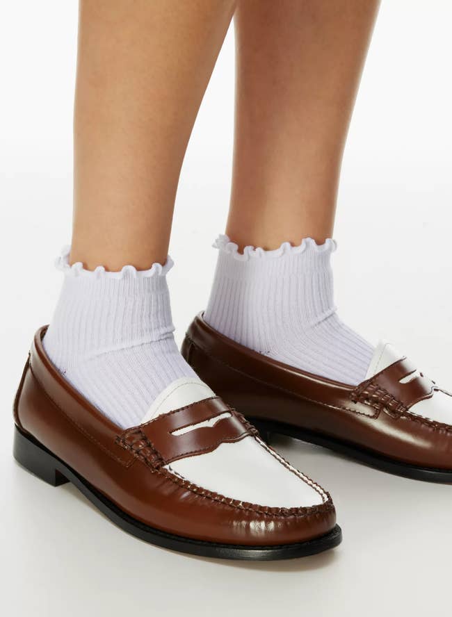 Person standing in frill-top socks and shiny brown loafers, focus on footwear. Ideal for smart-casual attire