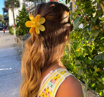 Model wearing a yellow daisy shaped claw clip in the back of their hair 