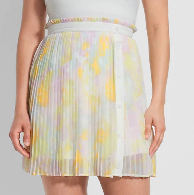Model is wearing a white skirt with a sheer pleated overlay with yellow splotches throughout