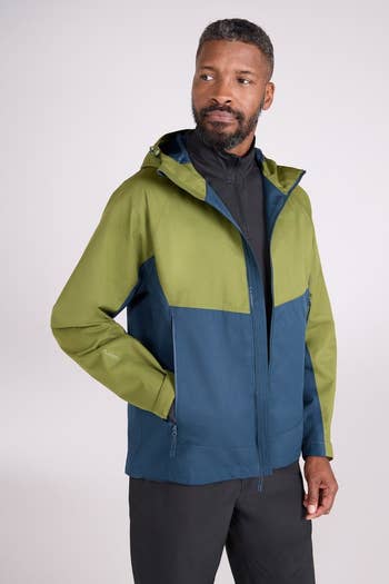 Person wearing a stylish two-tone outdoor jacket with a hood, looking to the side. The jacket is suitable for outdoor activities