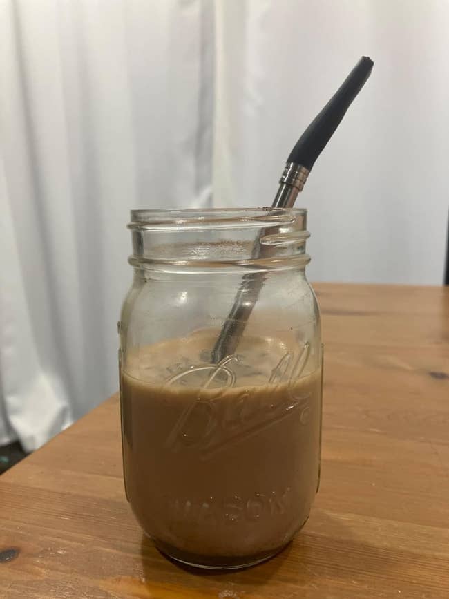 Mason jar with iced java  and a stainless alloy  straw connected  a woody  table
