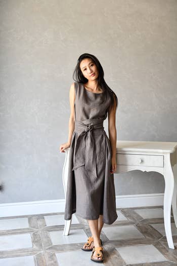 Person successful  a sleeveless, belted linen formal  and sandals stands beside a achromatic  table, offering a casual look