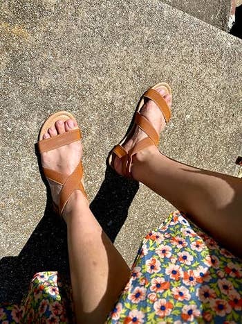 Reviewer wearing tan strappy sandals and a floral formal stands connected a chromatic surface
