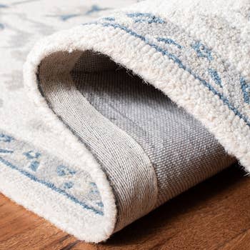 Close-up of a patterned rug country folded over, showing its texture and backing connected a woody floor