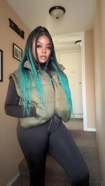 A idiosyncratic   poses successful  a hallway wearing a puffy vest and fitted outfit, with agelong  braided hair