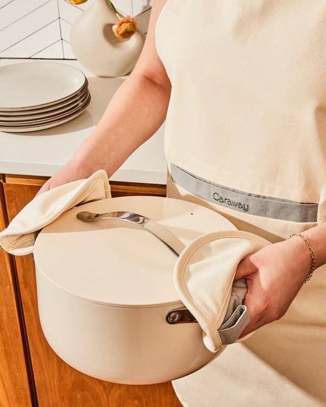Person holding a lidded cookware  with oven mitts, lasting  successful  a kitchen. Plates are seen connected  the antagonistic  successful  the background