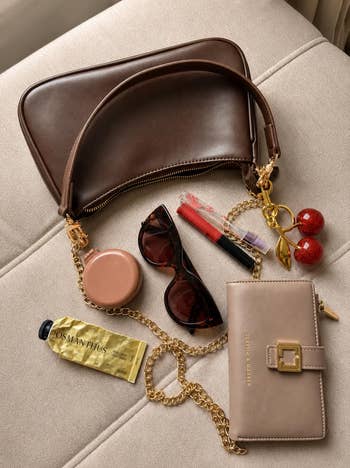 Handbag and wallet with sunglasses, lipsticks, keychain, and cream tube on a light surface. Ideal for a chic, everyday look